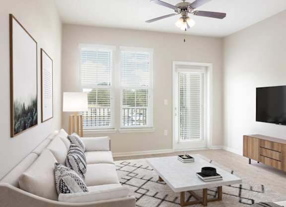 A living room with a grey couch, a coffee table, a flat screen TV, and a ceiling fan.