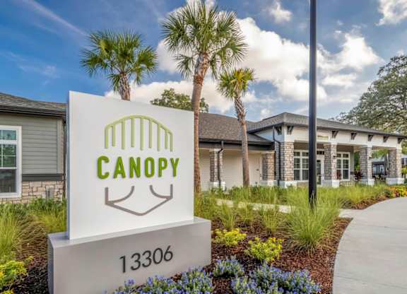 A sign for Canopy with a house in the background.