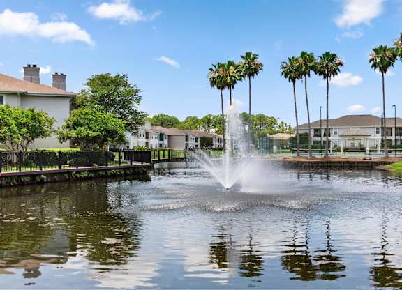 A fountain in the middle of a pond surrounded by palm trees.