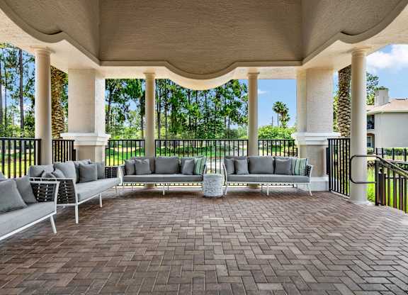 A patio with a white couch and a table with a vase on it.