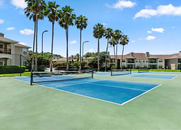 A tennis court surrounded by palm trees and apartment buildings.