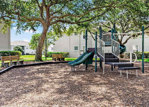 A playground with a green slide and a tree.