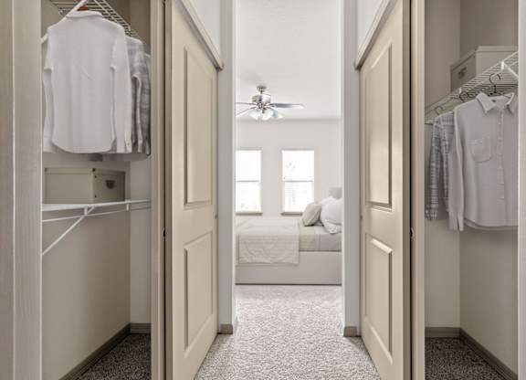 A white bedroom with a bed, a ceiling fan, and a closet with clothes hanging.