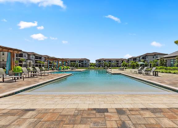 A large swimming pool surrounded by a brick patio and lounge chairs.