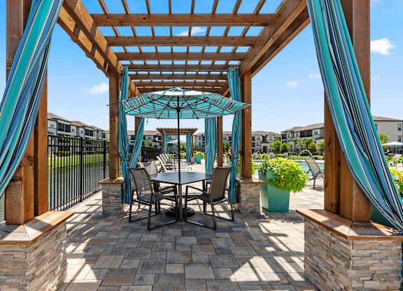 A patio with a table and chairs under a wooden pergola.