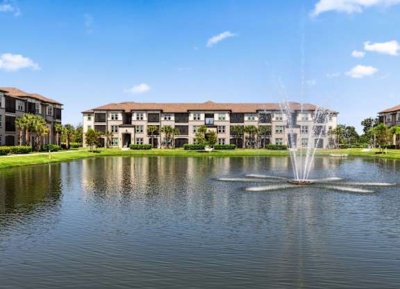 A fountain in the middle of a lake in front of a building.