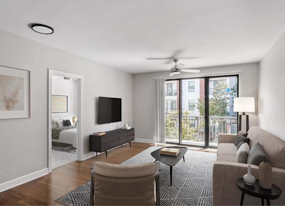 A living room with a television, a couch, a chair, a table, and a fan.