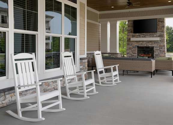 A row of white rocking chairs are lined up in front of a fireplace.