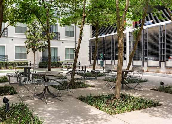 A patio with a table surrounded by chairs and trees.