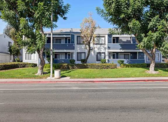 A street view of a residential area with apartment buildings and trees.