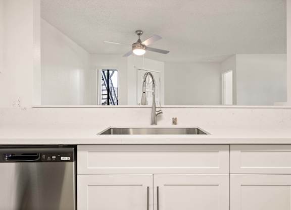 A white kitchen with a stainless steel dishwasher and a silver sink.