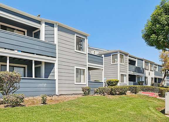A row of grey and blue houses with green lawns in front.
