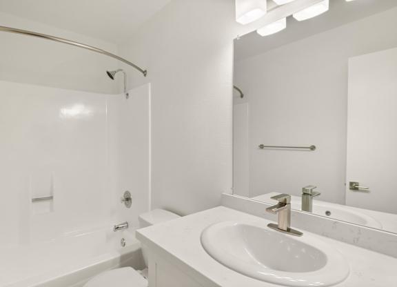 A white bathroom with a sink, mirror, and bathtub.
