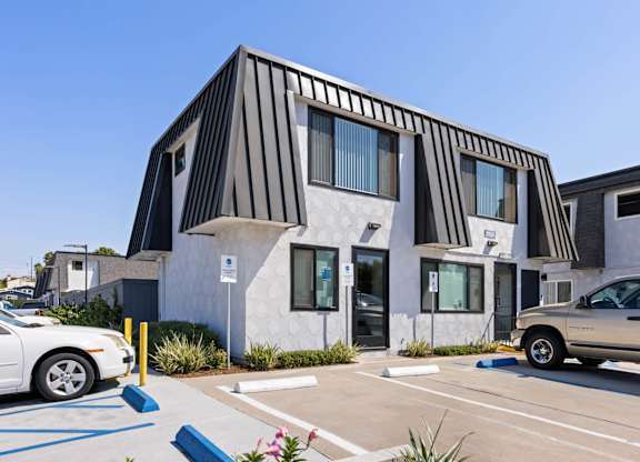 A white car is parked in a parking lot in front of a building with a black and white striped facade.