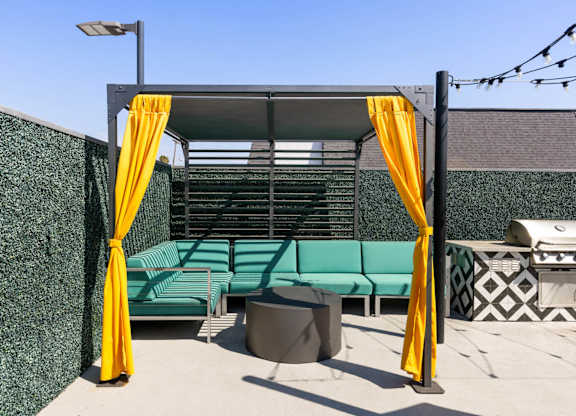 A patio area with a green couch and yellow curtains.