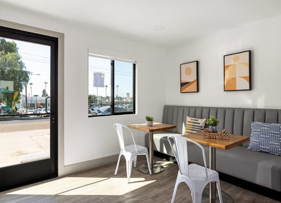 A white chair is in front of a grey couch with a table and two chairs in between.