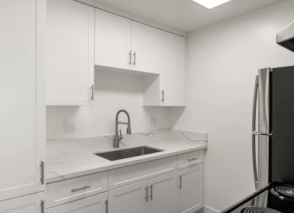 A kitchen with white cabinets and a black refrigerator.