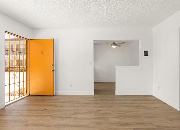 A room with a wooden floor and white walls, with a ceiling fan and a door leading to a balcony.