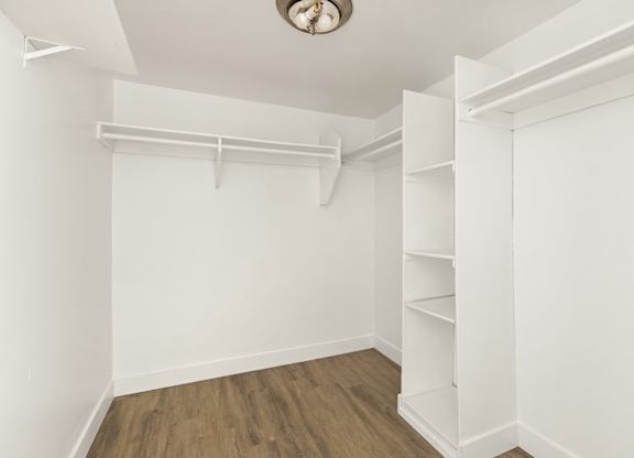 A white room with a wooden floor and a white closet with shelves.