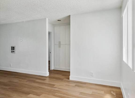 A room with white walls and wooden flooring with a doorway leading to another room.