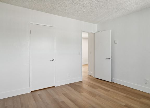 A room with white walls and wooden flooring with two doors.