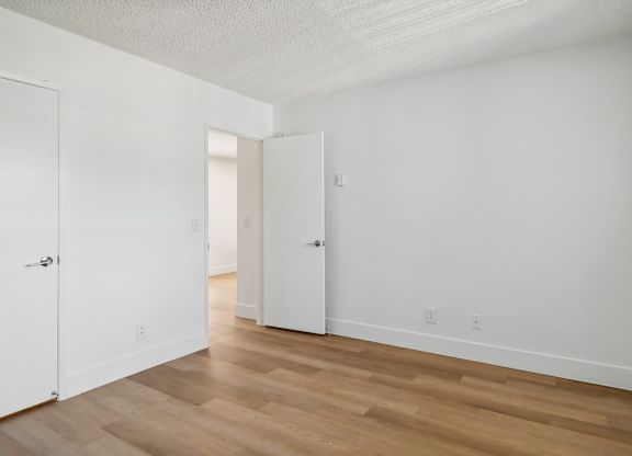 A room with white walls and wooden flooring with two doors.