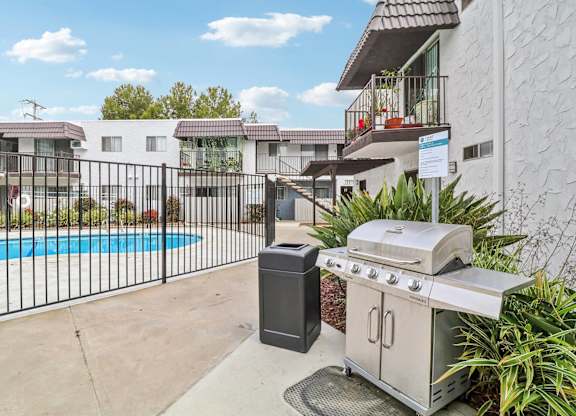 A BBQ grill and trash bin are on a patio next to a pool.