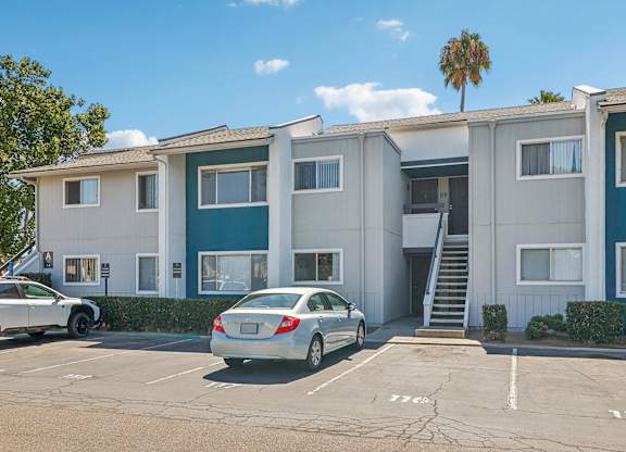 A car is parked in front of a two-story apartment building.