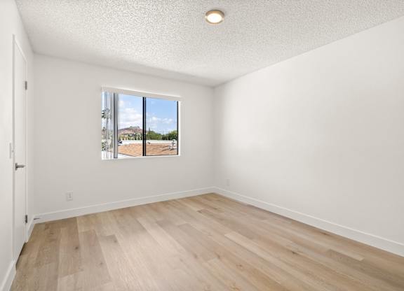 Empty room with wooden floor and a window showing an outdoor view.