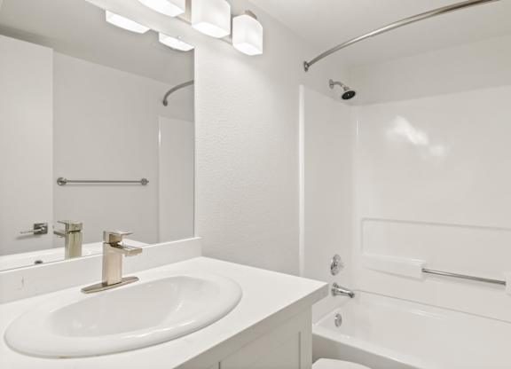 A white bathroom with a sink, mirror, and shower.