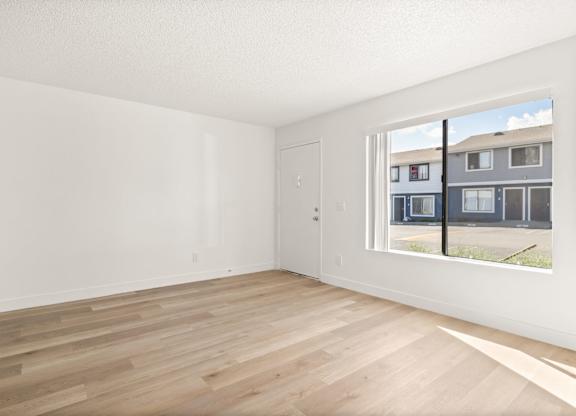 Empty room with wooden flooring and a window showing a building outside.