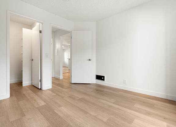 A room with white walls and wooden flooring with two open doors.
