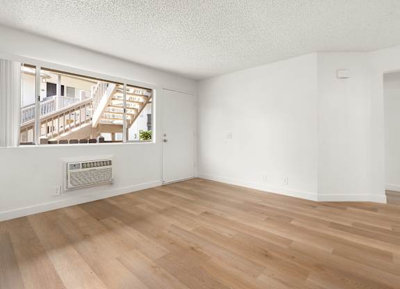 A room with wooden flooring and a window overlooking a balcony.
