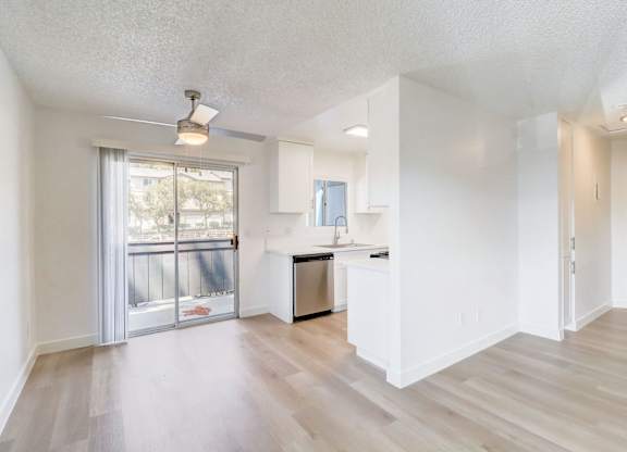 A spacious, empty room with a kitchenette and sliding glass doors leading to a balcony.