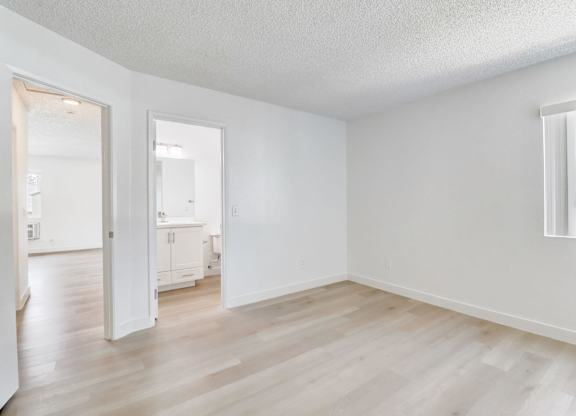 A room with white walls and wooden flooring, with a window showing a building outside.