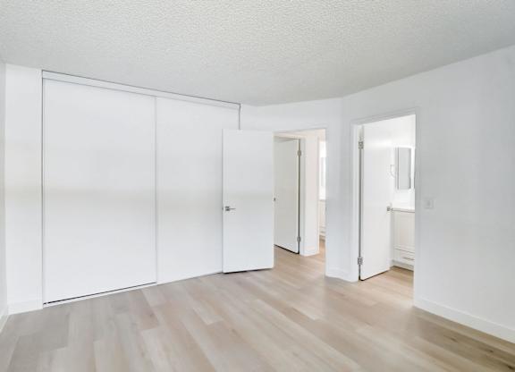 A room with white walls and wooden flooring with three white doors.