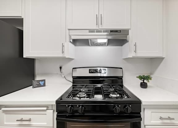 A black stove top oven with four burners and a silver range hood above it.
