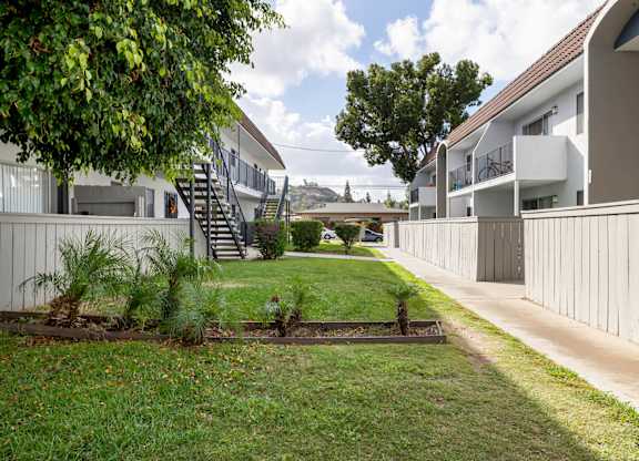 A grassy area in front of a building with a tree and a small garden.