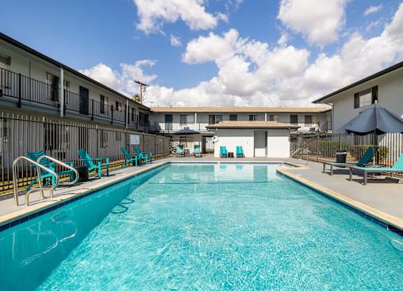 A large swimming pool in front of a building with lounge chairs and umbrellas.