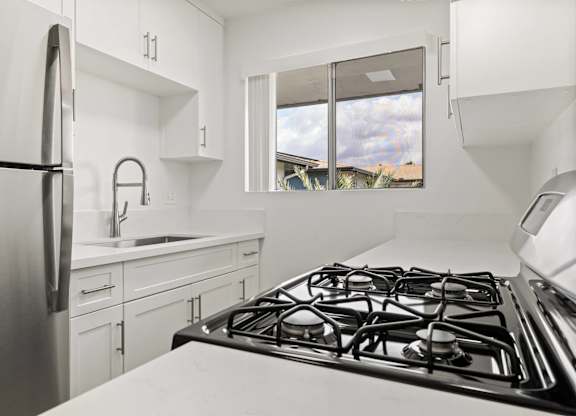 A modern kitchen with a stainless steel refrigerator, a stove, and white cabinets.