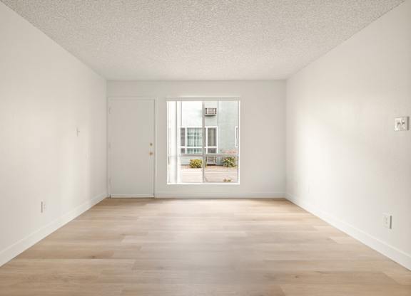A room with a white door and a window showing a balcony with plants.