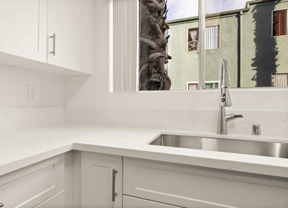 A kitchen with white cabinets and a silver sink.