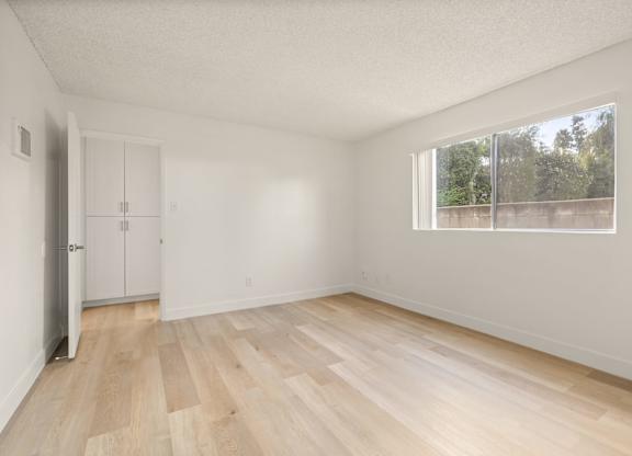 A room with wooden flooring and a window overlooking a fence.