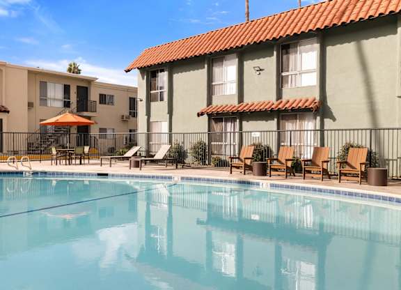A swimming pool in front of a building with a red tile roof.