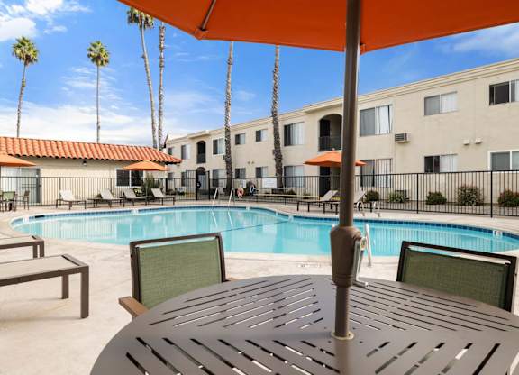 A pool area with a table and chairs under an umbrella.