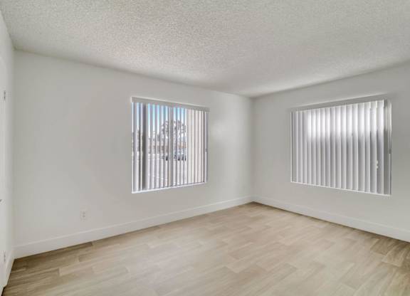A room with wooden flooring and two windows with blinds.