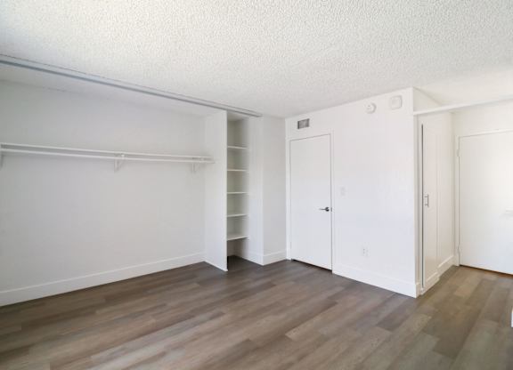 A room with white walls and wooden flooring with a closet and a door.