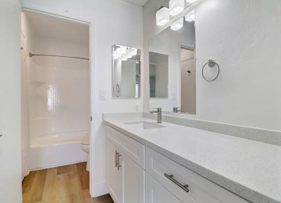 A white bathroom with a sink, mirror, and shower.