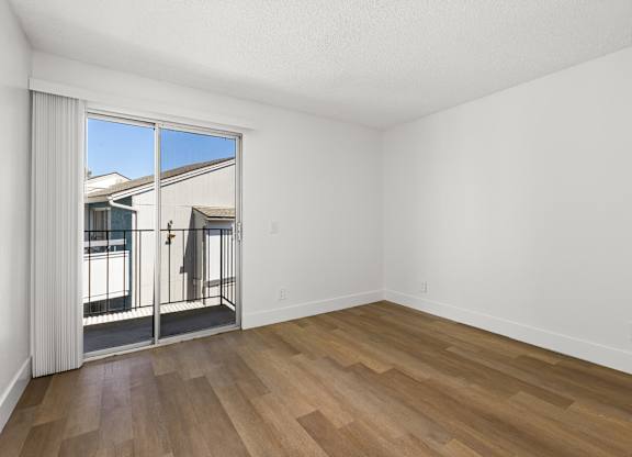 A room with wooden flooring and a large window overlooking a balcony.