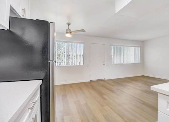 A black fridge in a kitchen with white cabinets and a wooden floor.